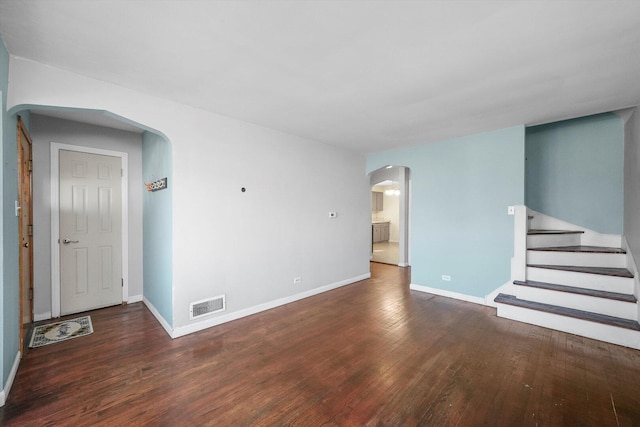 unfurnished living room featuring hardwood / wood-style floors, arched walkways, visible vents, and baseboards