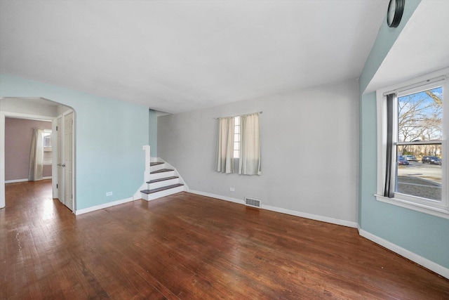 unfurnished room featuring plenty of natural light, arched walkways, visible vents, and wood-type flooring