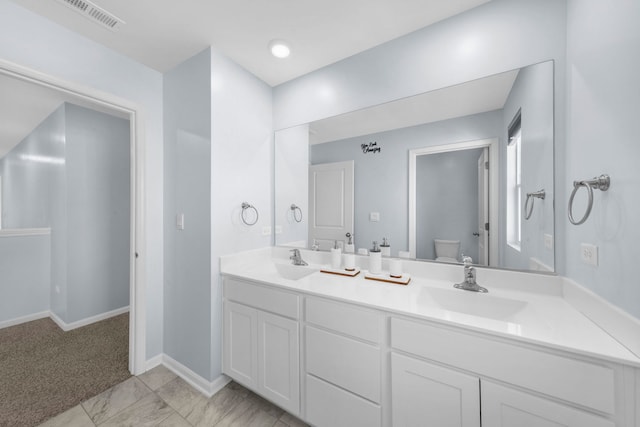 bathroom with visible vents, baseboards, toilet, double vanity, and a sink