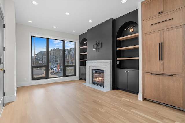 unfurnished living room with light wood finished floors, baseboards, built in features, a premium fireplace, and recessed lighting