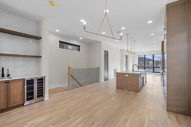 kitchen with brown cabinets, a kitchen island with sink, light wood-style flooring, a sink, and wine cooler