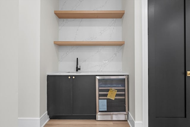 bar featuring beverage cooler, decorative backsplash, a sink, light wood finished floors, and indoor wet bar