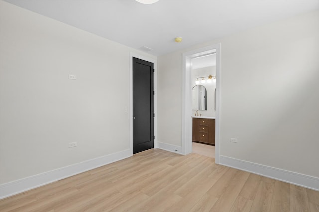 unfurnished bedroom featuring light wood-type flooring, baseboards, visible vents, and ensuite bath