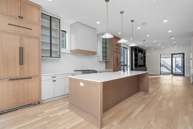 kitchen featuring light wood-type flooring, an island with sink, paneled built in fridge, light countertops, and custom exhaust hood