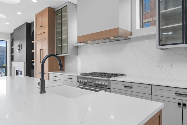 kitchen featuring stainless steel range, custom range hood, light stone countertops, and backsplash