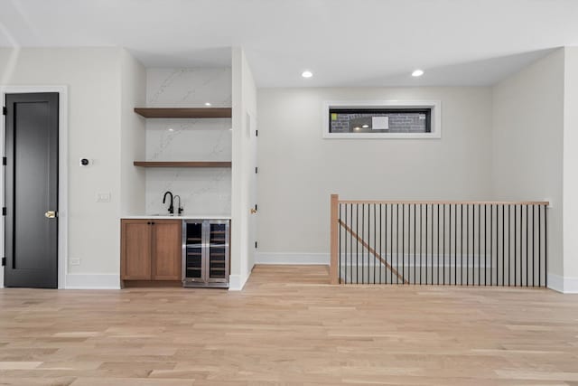 bar with light wood-type flooring, wet bar, baseboards, and beverage cooler