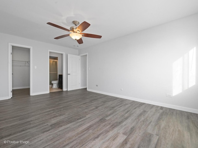 unfurnished bedroom featuring a walk in closet, baseboards, and dark wood-type flooring