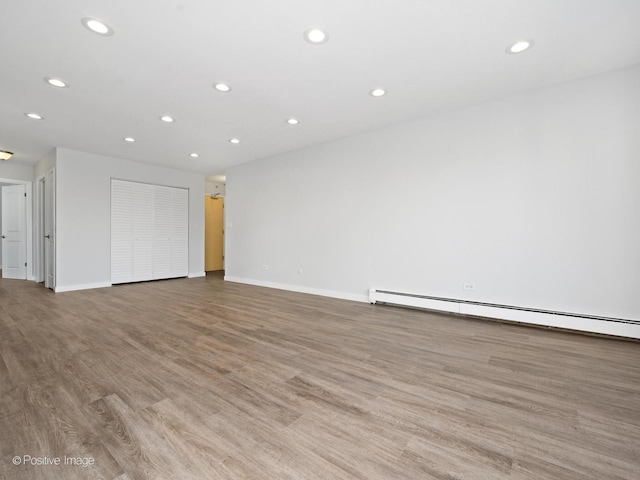 unfurnished living room with recessed lighting, a baseboard heating unit, and light wood-style flooring