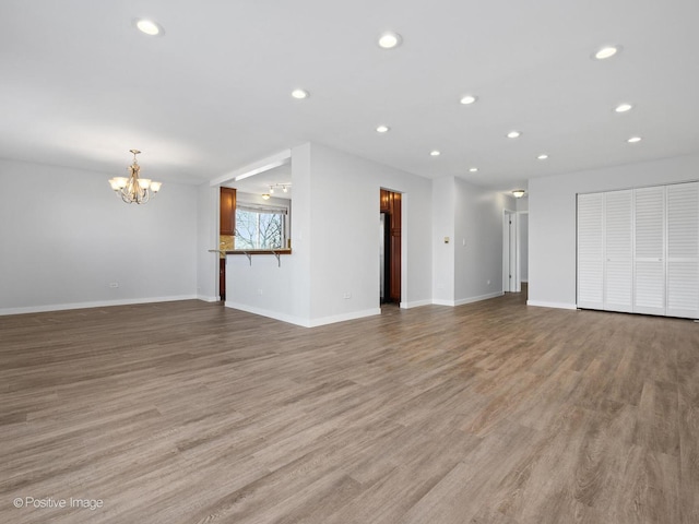 unfurnished living room featuring a chandelier, recessed lighting, baseboards, and light wood-style floors