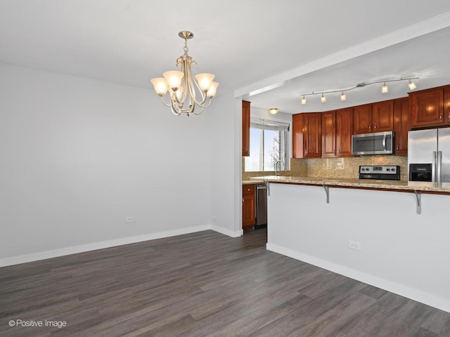 kitchen with backsplash, a chandelier, dark wood finished floors, a breakfast bar area, and appliances with stainless steel finishes