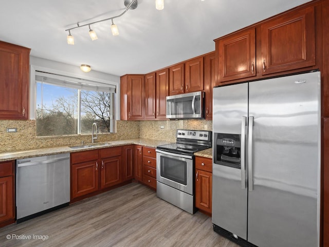 kitchen with light wood-style flooring, a sink, light stone counters, appliances with stainless steel finishes, and decorative backsplash