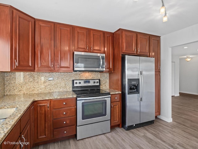 kitchen featuring tasteful backsplash, baseboards, light wood-type flooring, light stone counters, and appliances with stainless steel finishes