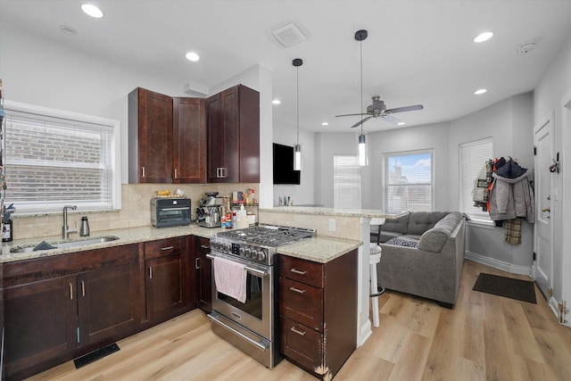 kitchen featuring visible vents, a peninsula, a sink, high end stove, and tasteful backsplash