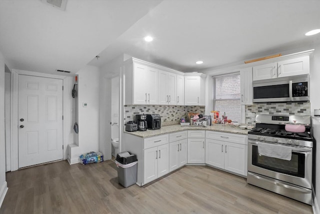 kitchen featuring visible vents, white cabinets, stainless steel appliances, and light wood-type flooring