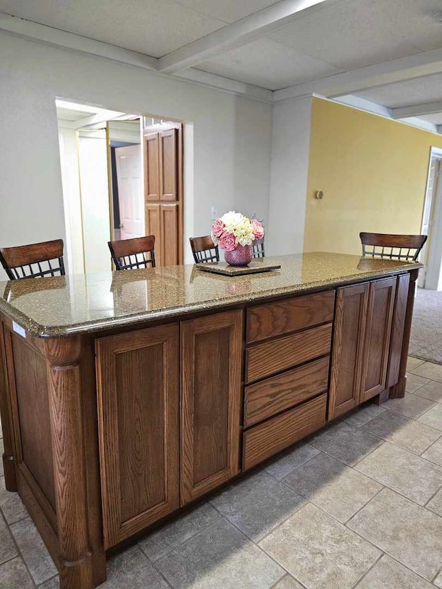 400 S 2nd St, Wapella, IL 61777 - kitchen with beam ceiling, a center island, stone countertops, stone tile flooring, and brown cabinets