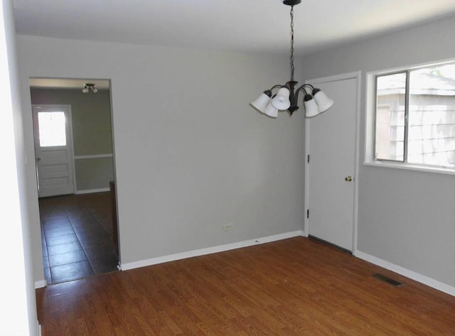 unfurnished dining area featuring a notable chandelier, baseboards, visible vents, and wood finished floors