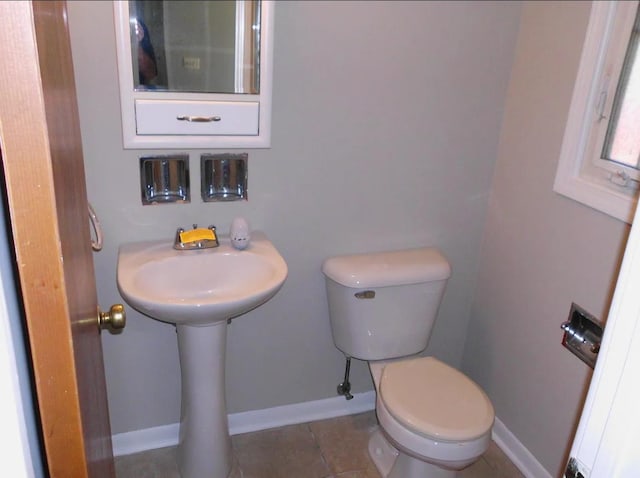 half bath with baseboards, toilet, and tile patterned flooring