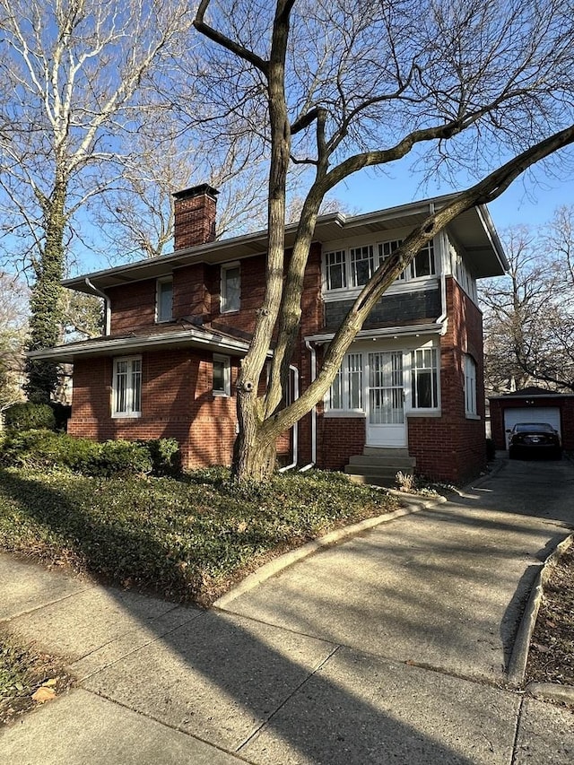 view of front of house featuring brick siding, a chimney, a detached garage, and an outdoor structure