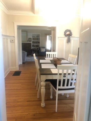 dining room featuring beamed ceiling, light wood-style flooring, and ornamental molding