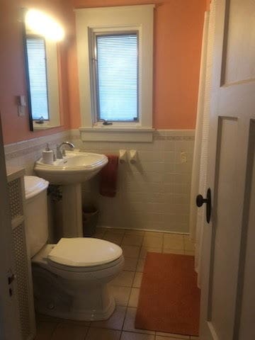 half bath featuring a wainscoted wall, toilet, tile walls, and tile patterned flooring