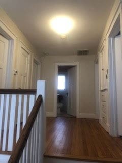 hall featuring wood finished floors, an upstairs landing, and baseboards