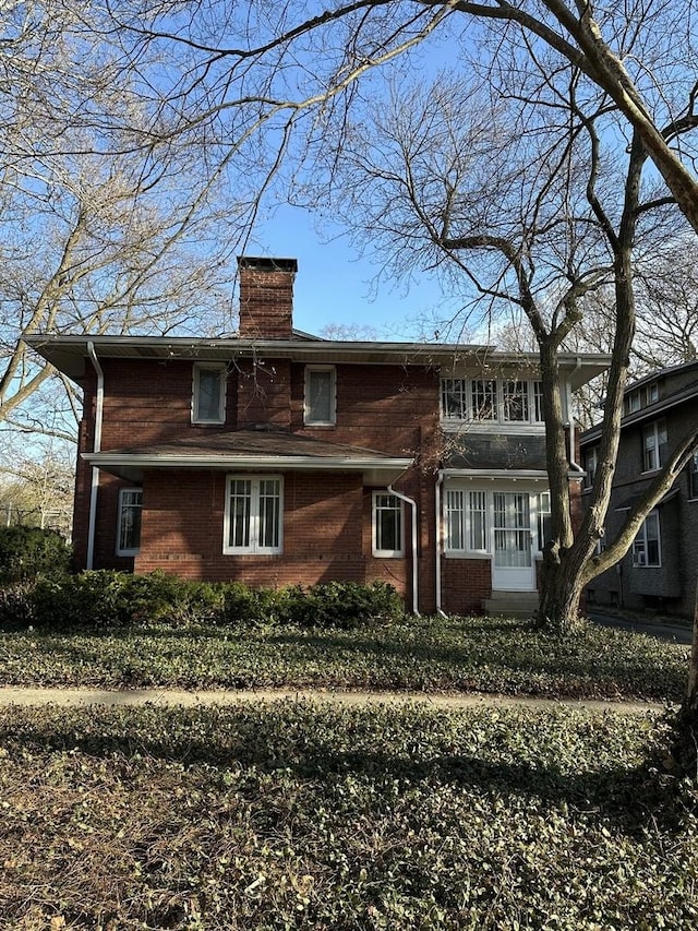 back of house with brick siding and a chimney