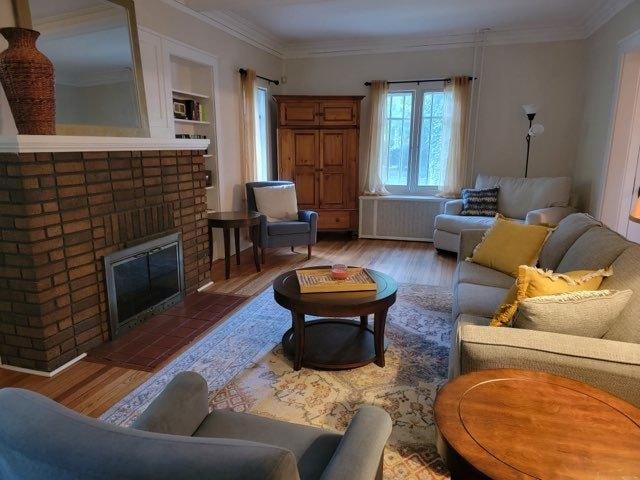 living area featuring built in features, a brick fireplace, wood finished floors, and crown molding