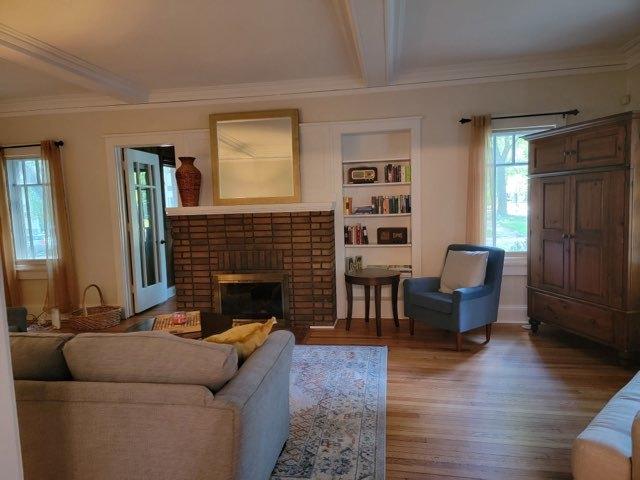 living room with built in shelves, wood finished floors, a fireplace, ornamental molding, and beamed ceiling