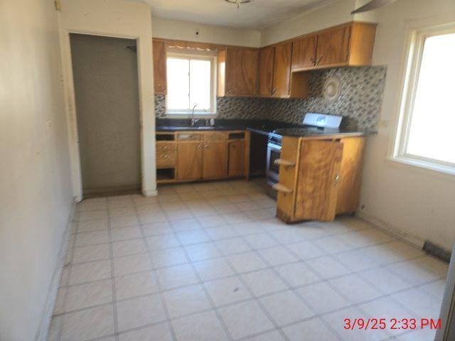 kitchen featuring brown cabinetry, a sink, backsplash, and range with two ovens