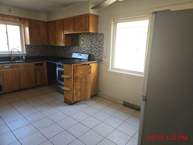 kitchen with dark countertops, backsplash, brown cabinets, stainless steel appliances, and a sink