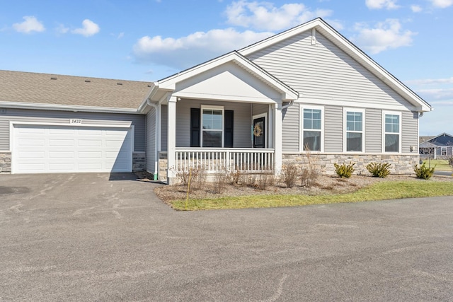 view of front facade featuring an attached garage, covered porch, stone siding, and driveway