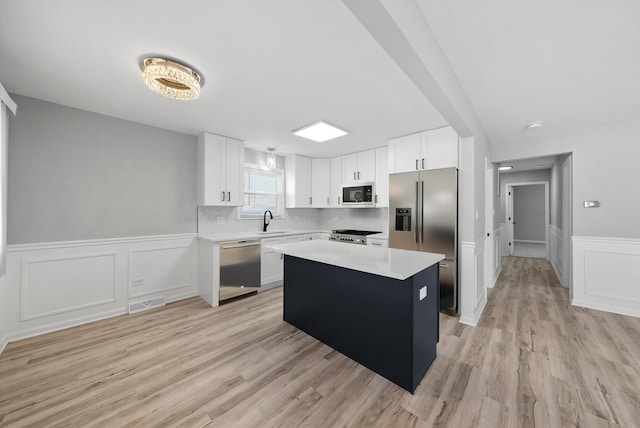 kitchen with a sink, stainless steel appliances, light countertops, white cabinetry, and a center island