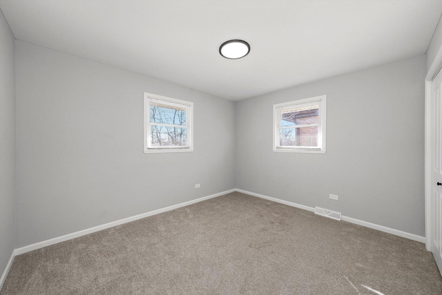 empty room with a wealth of natural light, visible vents, carpet floors, and baseboards