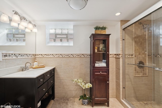 full bath with tile walls, a stall shower, vanity, and tile patterned flooring