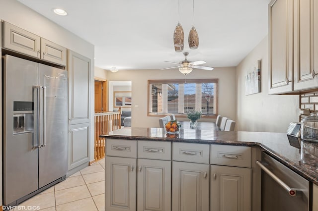 kitchen featuring a ceiling fan, stainless steel appliances, dark stone counters, a peninsula, and light tile patterned floors