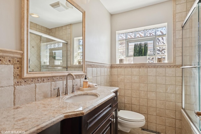 bathroom with vanity, visible vents, a tile shower, tile walls, and toilet