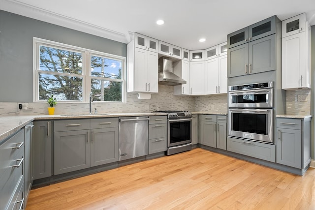 kitchen with gray cabinetry, stainless steel appliances, wall chimney exhaust hood, and a sink