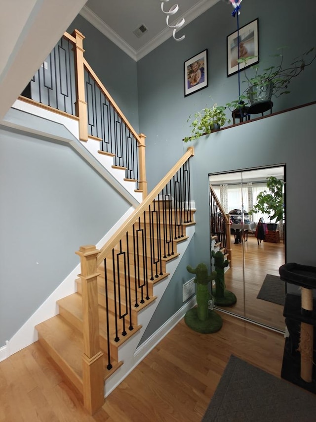 stairs featuring wood finished floors, visible vents, baseboards, a towering ceiling, and crown molding