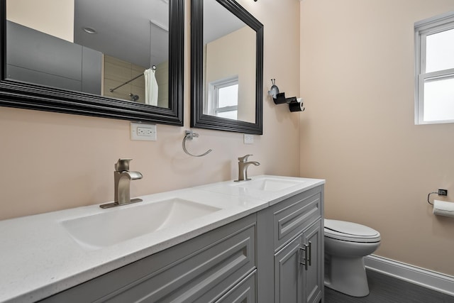 bathroom featuring double vanity, toilet, baseboards, and a sink