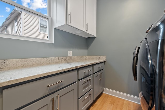 laundry room featuring baseboards, cabinet space, washer / dryer, and light wood finished floors