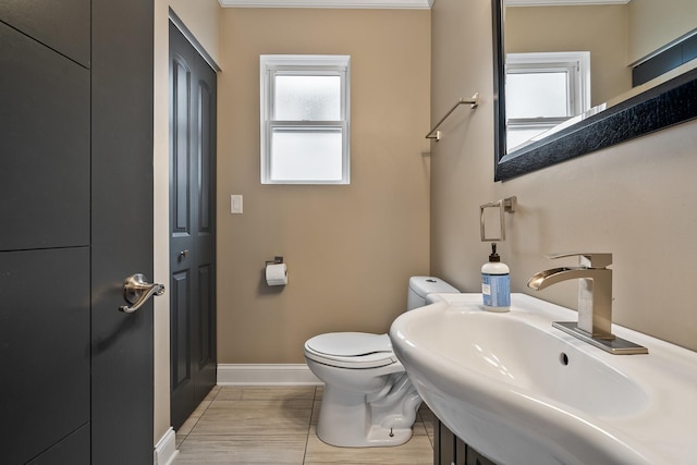 half bathroom with toilet, baseboards, and a sink