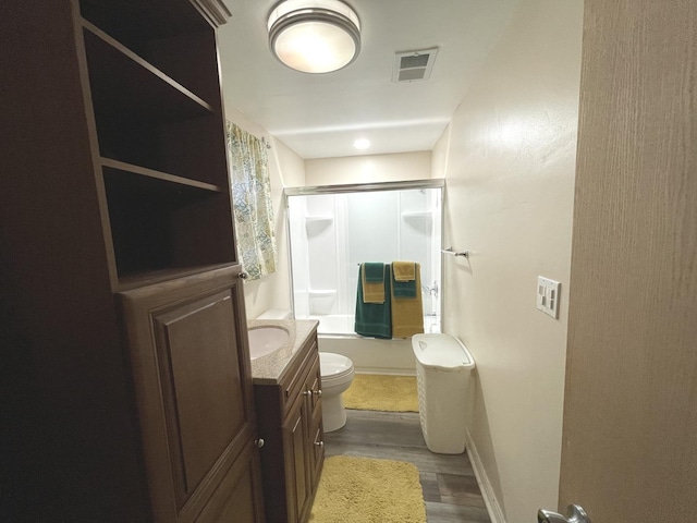 bathroom featuring vanity, wood finished floors, visible vents, bath / shower combo with glass door, and toilet