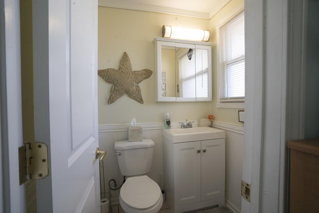 half bath with crown molding, toilet, wainscoting, a decorative wall, and vanity