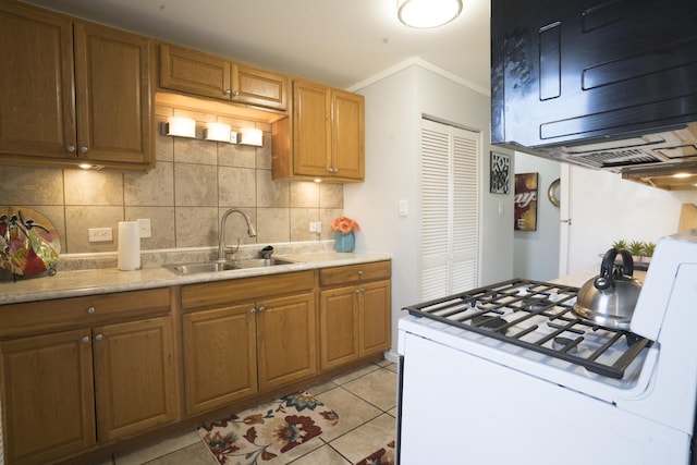 kitchen featuring gas range gas stove, light tile patterned flooring, a sink, decorative backsplash, and light countertops