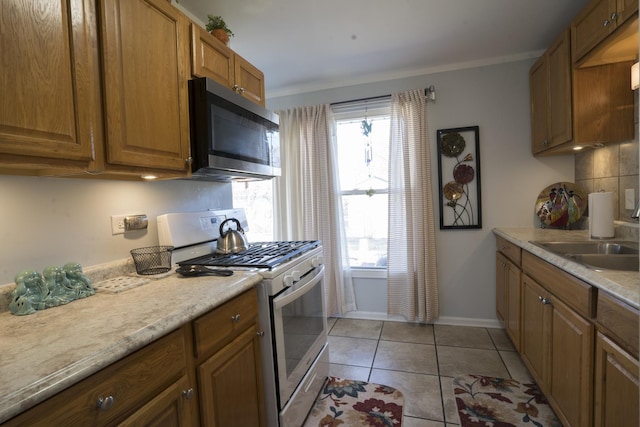 kitchen with light tile patterned flooring, a sink, light countertops, white gas range oven, and stainless steel microwave