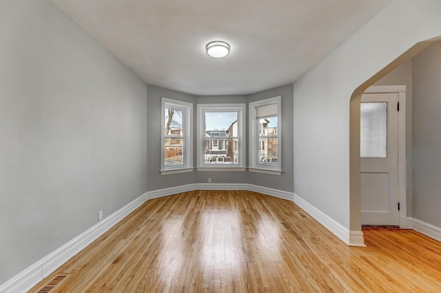 unfurnished room featuring arched walkways, visible vents, light wood-type flooring, and baseboards