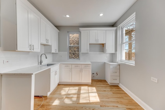 kitchen with light wood-style flooring, a sink, tasteful backsplash, white cabinetry, and baseboards