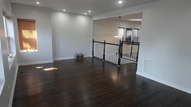 empty room with wood finished floors, visible vents, and baseboards