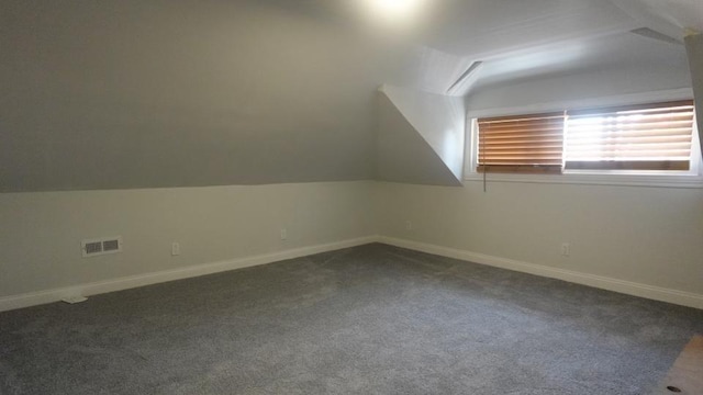 additional living space with dark colored carpet, visible vents, baseboards, and vaulted ceiling