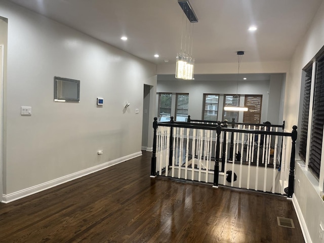 corridor featuring wood finished floors, visible vents, baseboards, recessed lighting, and an upstairs landing